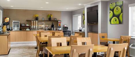 Un espace repas moderne avec des tables et des chaises en bois, une cuisine en arrière-plan et un mur orné d’une enseigne « La Quinta ».