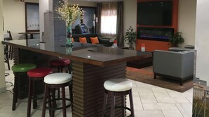 A modern bar area with stools, a large TV, and a decorative plant.