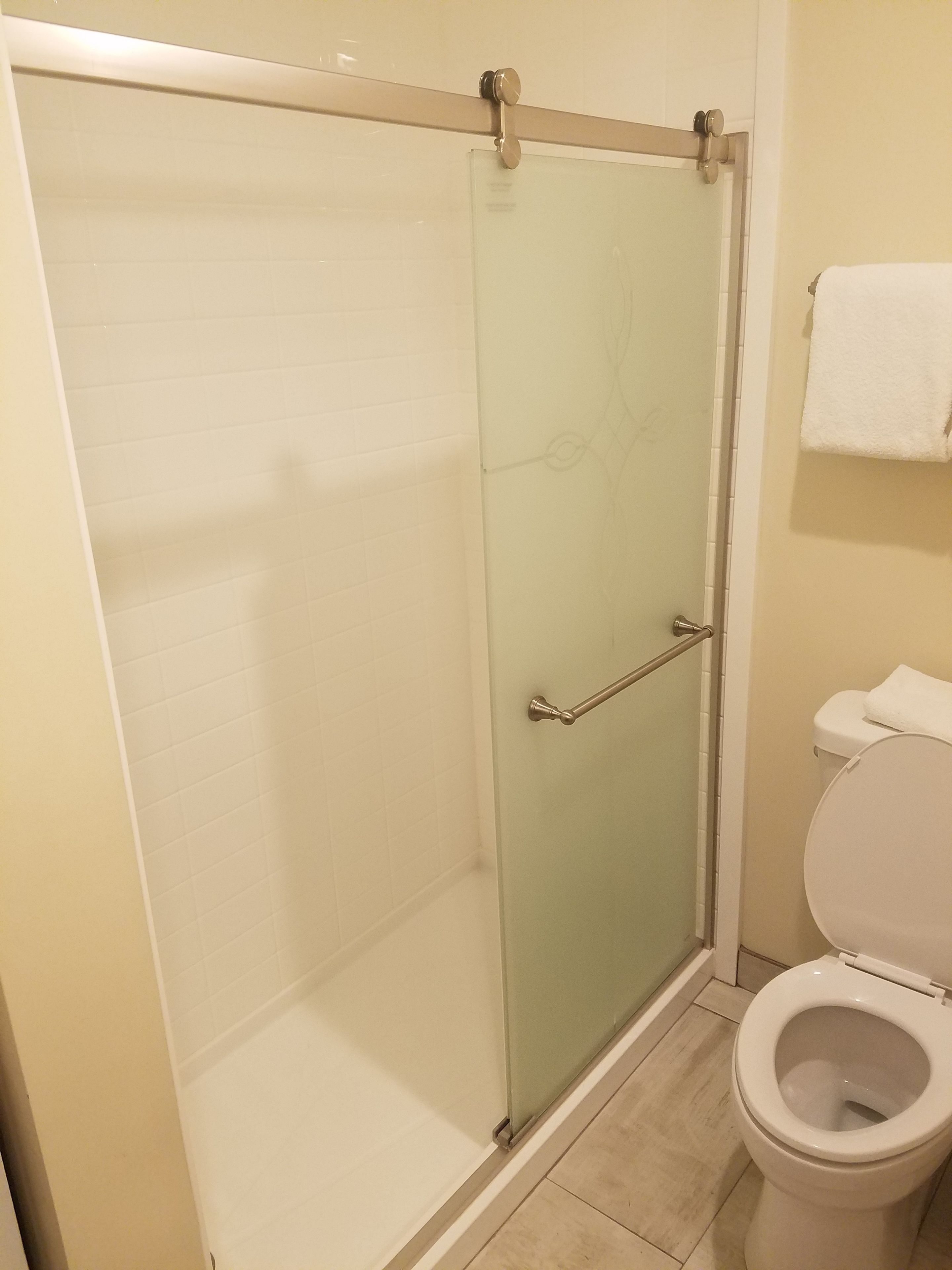 A glass-enclosed shower with a glass door, a toilet, and a towel hanging on the wall.