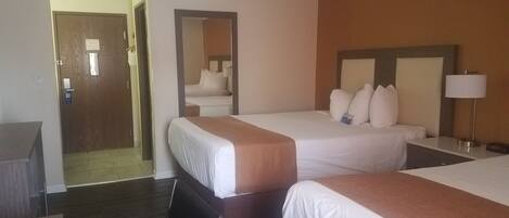 A hotel room with two beds, a desk, a chair, and a mirror.