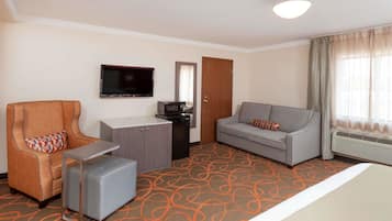 Habitación de hotel con sofá, sillón, pequeña mesa y televisión.