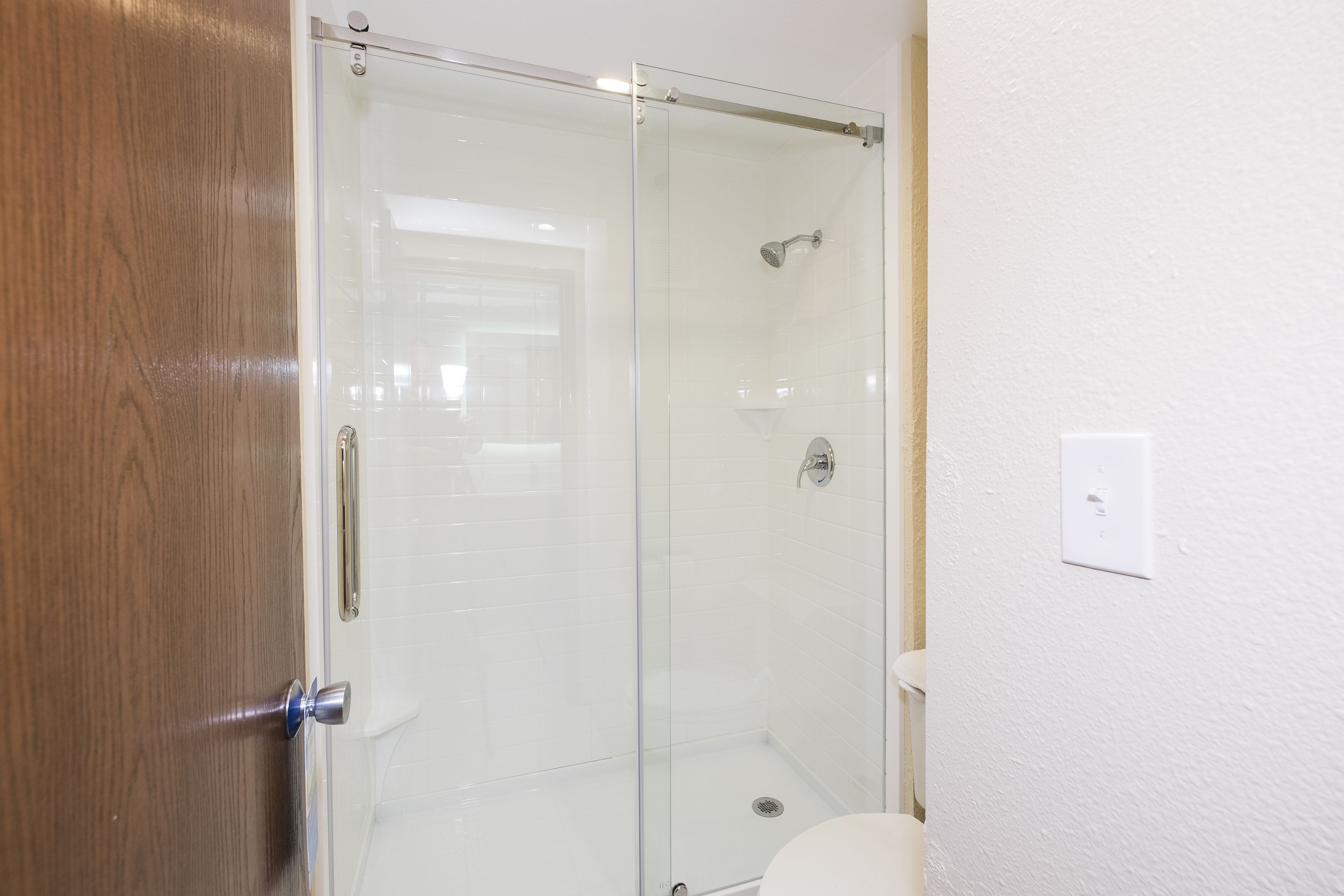 A glass-enclosed shower stall with a white toilet and a wooden door.