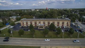 A large hotel with a central courtyard, multiple parking lots, and a surrounding landscape with trees and a distant lighthouse.