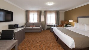 A hotel room with a bed, a sofa, a desk with a computer, a TV, and a window with curtains.
