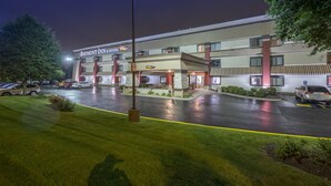 A hotel with a flat facade, a parking lot, and a well-lit entrance.
