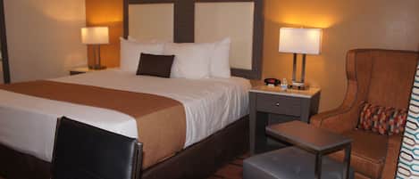 A hotel room with a large bed, two bedside tables with lamps, a small table, a chair, and a suitcase.