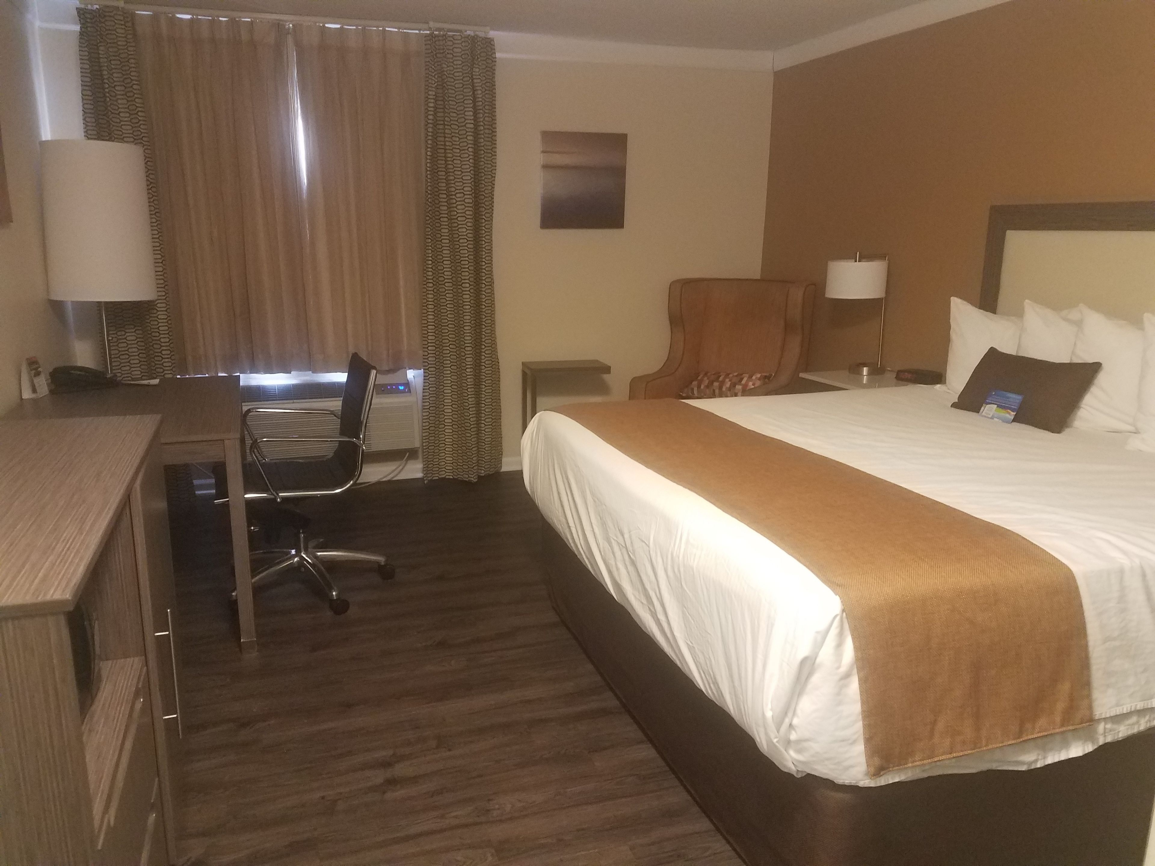 A hotel room with a bed, a desk, a chair, a lamp, and a window with curtains.