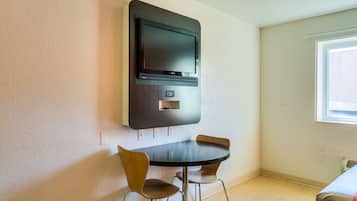 Une chambre moderne équipée d’un téléviseur à écran plat fixé au mur, d’une table ronde avec deux chaises et d’une fenêtre laissant entrer la lumière naturelle.