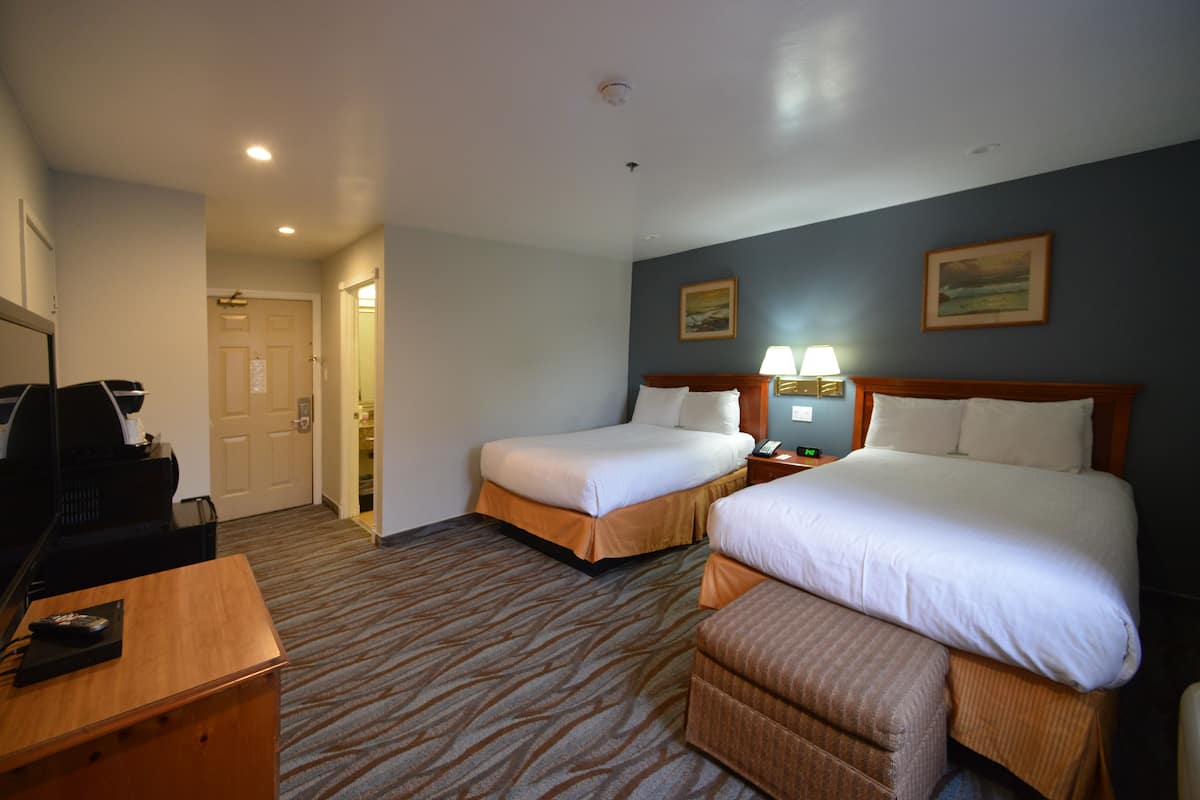 A hotel room with two beds, a desk, a chair, and a television.