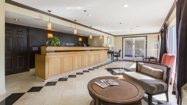 Eine Hotelhalle mit Empfangsschalter, Check-in-Bereich, einer Sitzecke mit Sofa und Sesseln sowie einem Schalter mit Computer und Telefon.