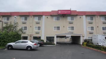 A multi-story hotel with a red roof and beige walls, featuring a parking lot with several cars.