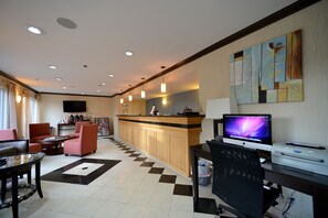 A hotel lobby with a reception desk, seating area, and a computer setup. - Cherry Orchard Inn (Sunnyvale)