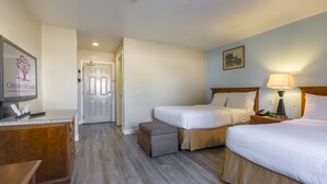 Ein Hotelzimmer mit zwei Betten, einem Schreibtisch, einem Fernseher und einer Lampe.