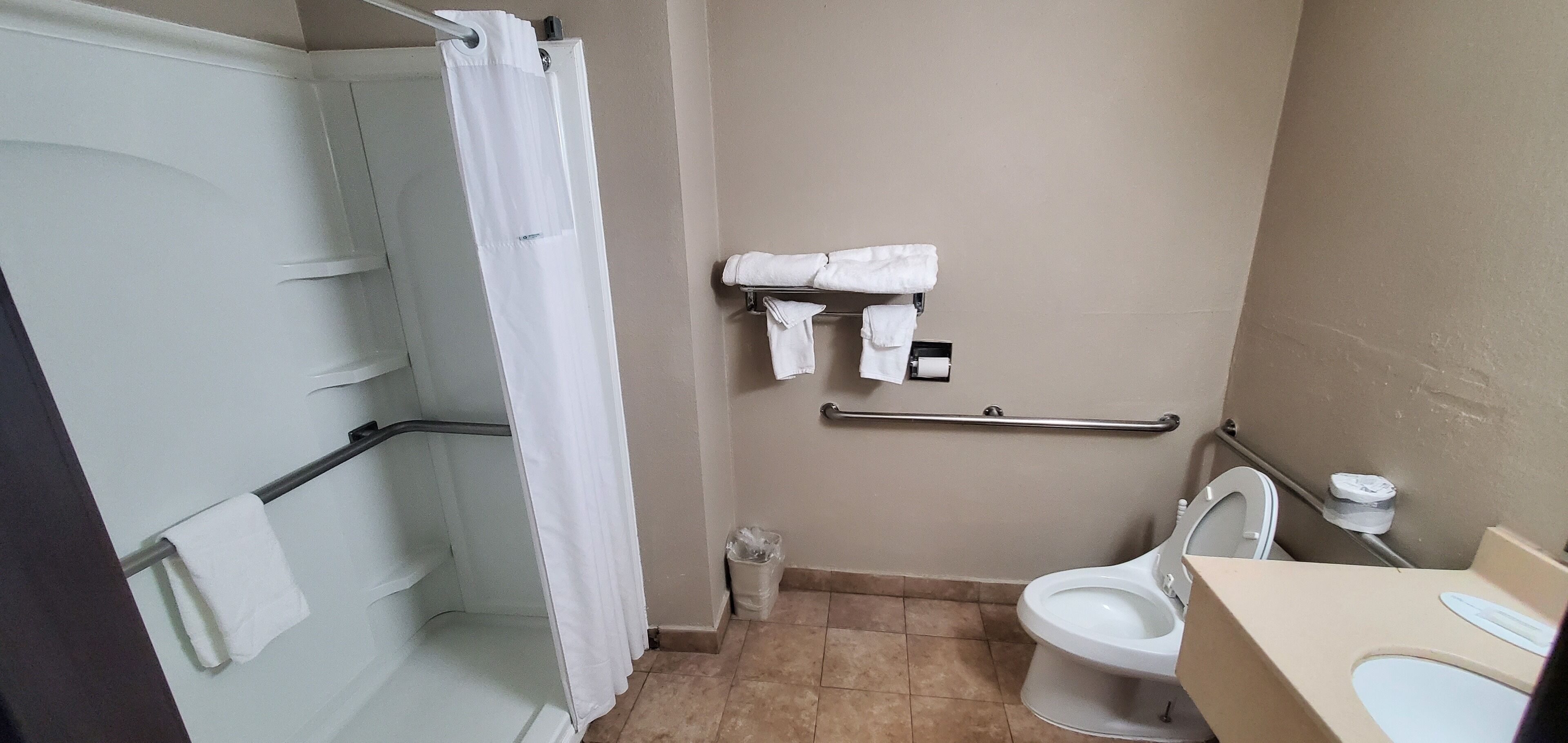 A bathroom with a shower, toilet, and a towel rack with towels.