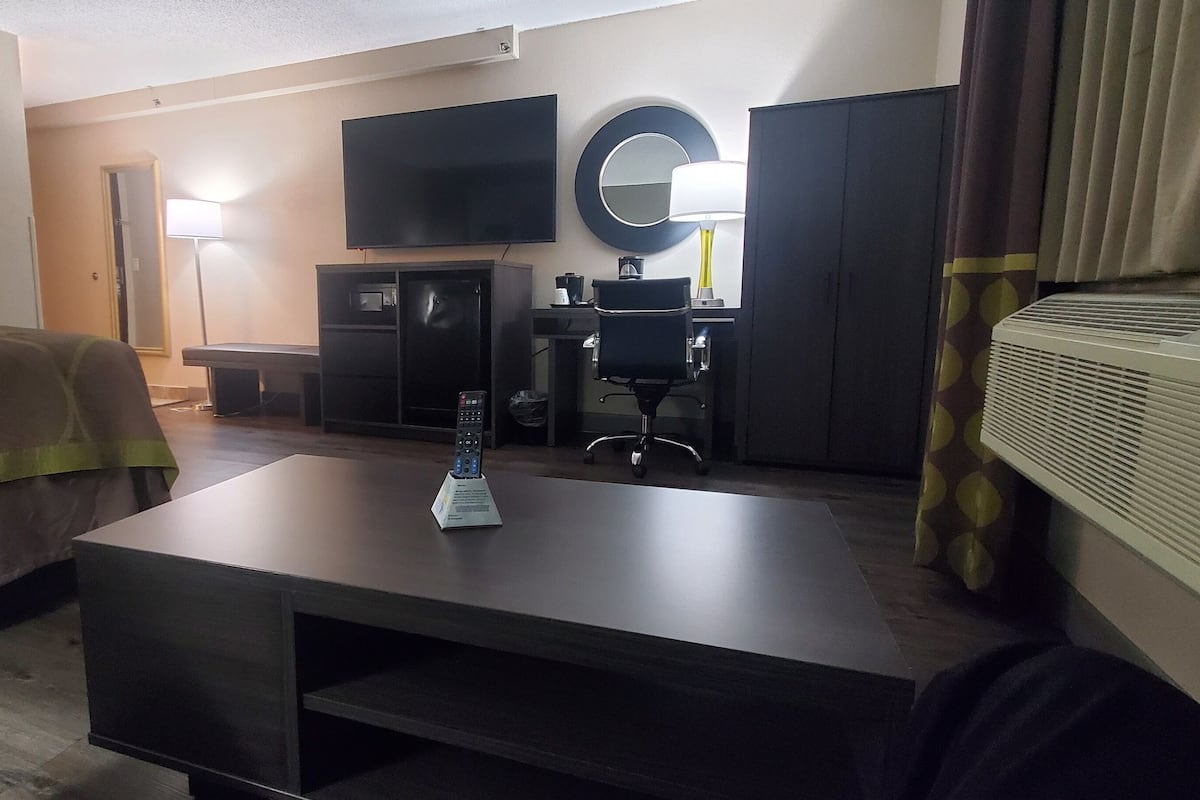 Ett hotellrum med en säng, ett skrivbord, en stol, en tv, en spegel och en lampa.