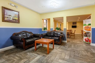 Un hall de hotel con dos sofás de cuero, una mesa de centro de madera, un cuadro en la pared, un área de comedor con sillas de madera y un cartel que anuncia el desayuno.