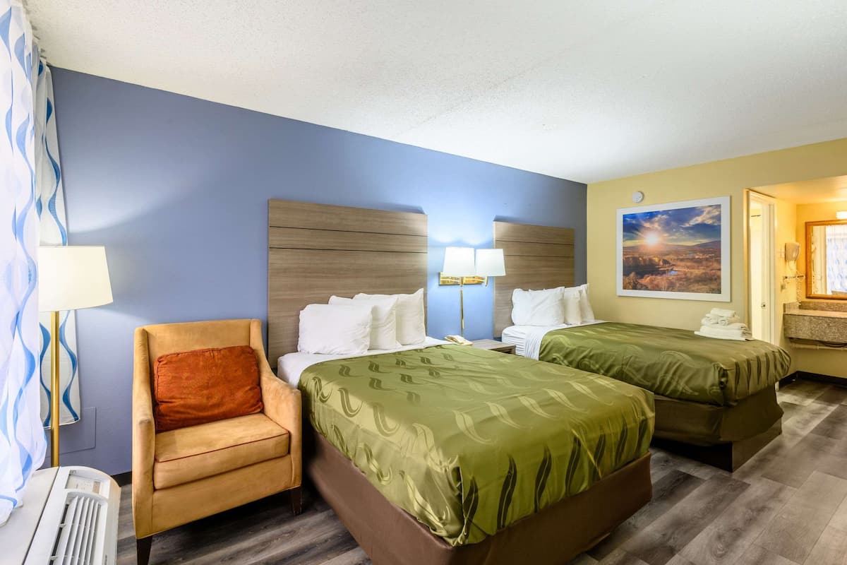 A hotel room with two beds, a chair, and a nightstand with lamps.