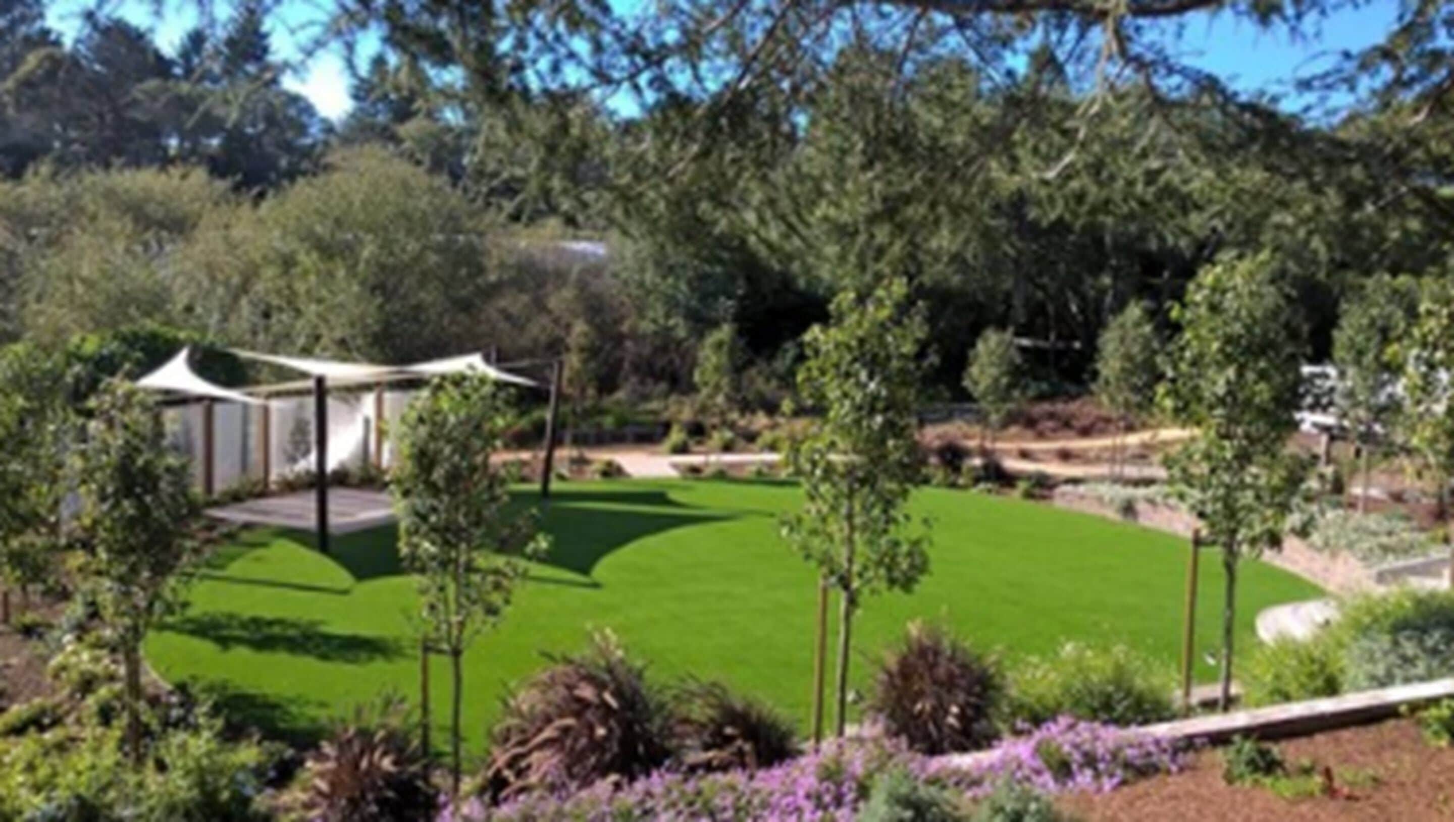 A well-maintained garden with a lawn, trees, and a white structure.