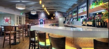 Zona de bar con sillas de madera, una barra con una presentación y estantes con botellas.