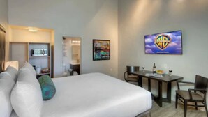 Ein Hotelzimmer mit einem Bett, einem Schreibtisch und einem Stuhl. An der Wand hängt ein Fernseher, über dem Schreibtisch ein Gemälde.