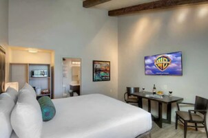 Habitación de hotel con una cama, un escritorio y una silla. Hay un televisor en la pared y un cuadro sobre el escritorio.
