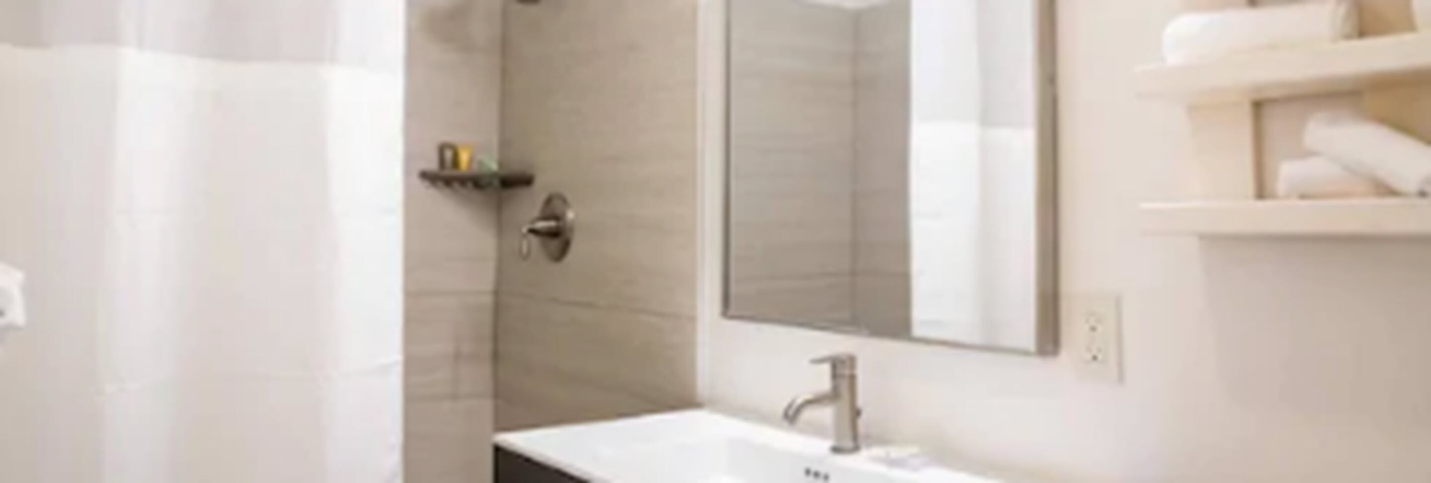 A modern bathroom with a white sink, a mirror, and a shower area.