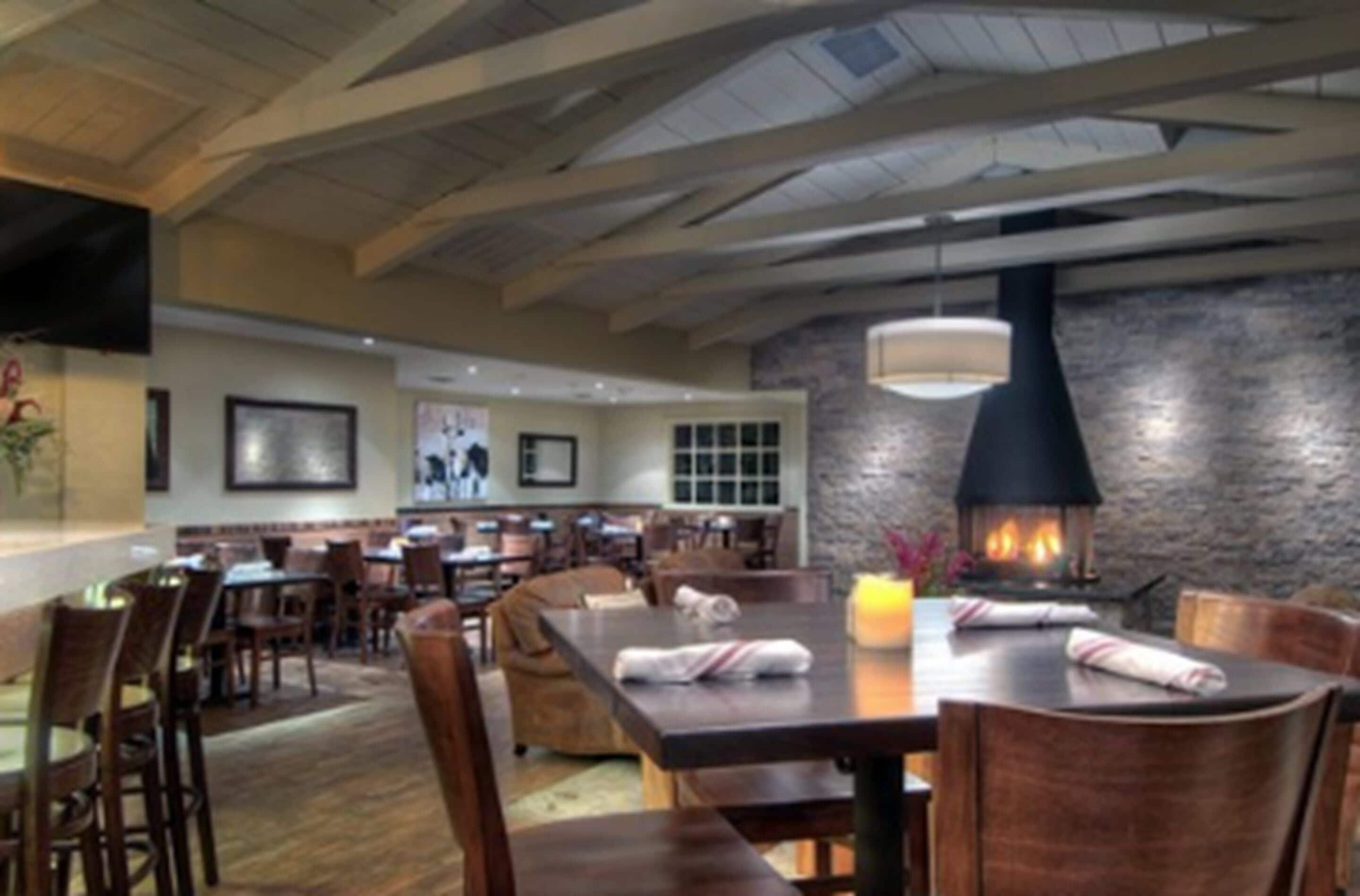A restaurant with wooden tables and chairs, a stone wall, and a fireplace.