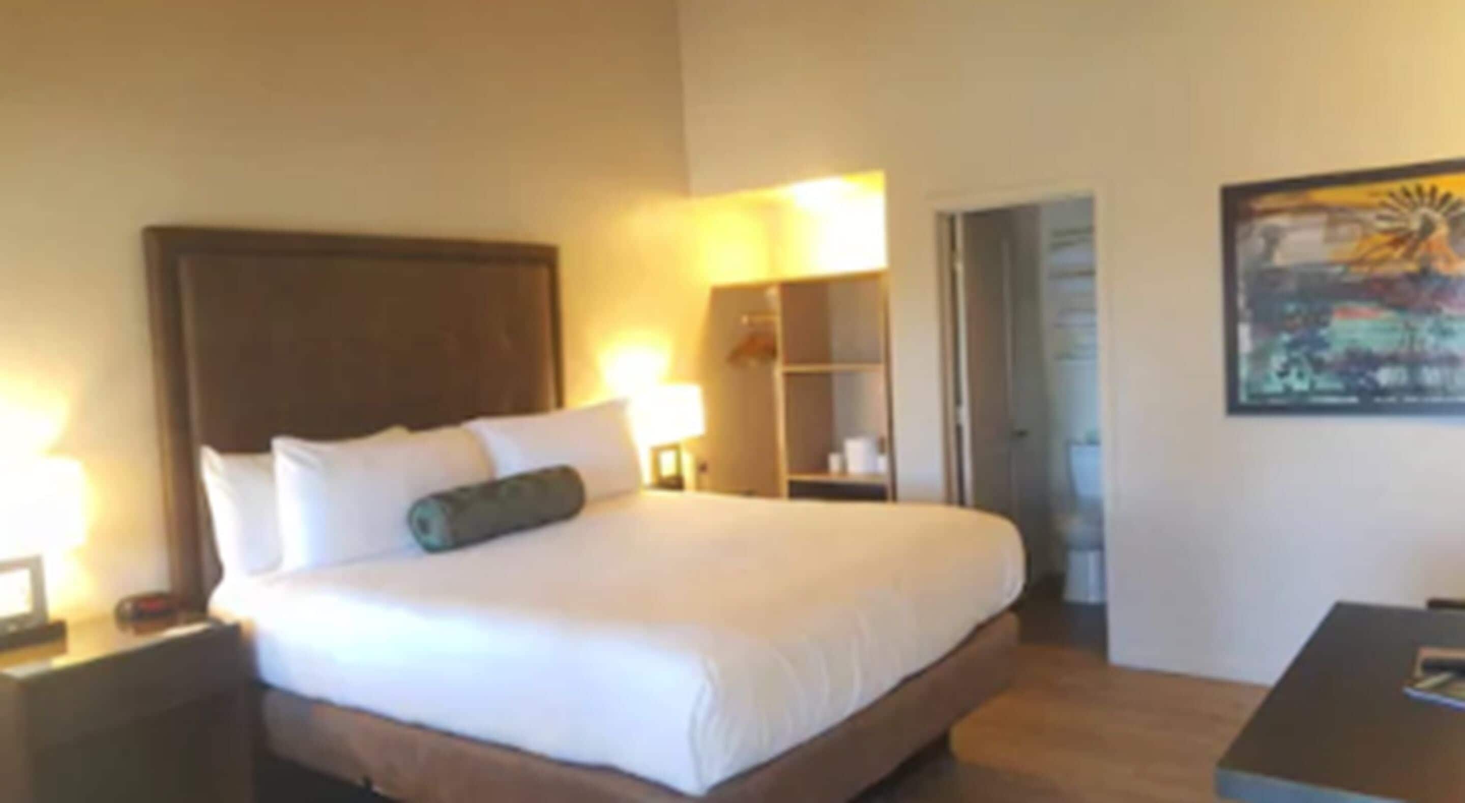 A hotel room with a large bed, bedside lamps, a nightstand, a small table, and a painting on the wall.