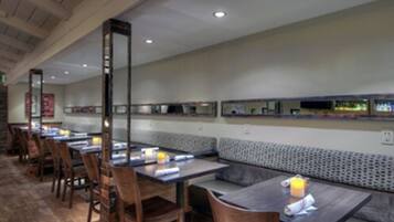 Un restaurant avec de longues tables et des banquettes, des chaises en bois et un mur décoré de motifs.