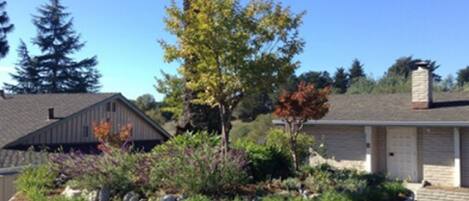 A residential building with a garage, a landscaped garden with various plants, and a tall tree in the foreground.