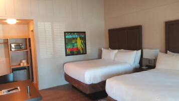 A hotel room with two beds, a desk, a microwave, and a painting on the wall.