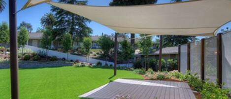 A landscaped outdoor area with a wooden deck, a grassy lawn, and a shaded area with a canopy.