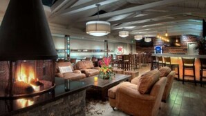 Ein gemütlicher Lounge-Bereich mit Kamin aus Stein, bequemen Sitzmöglichkeiten und einer Bar mit Neonreklame.