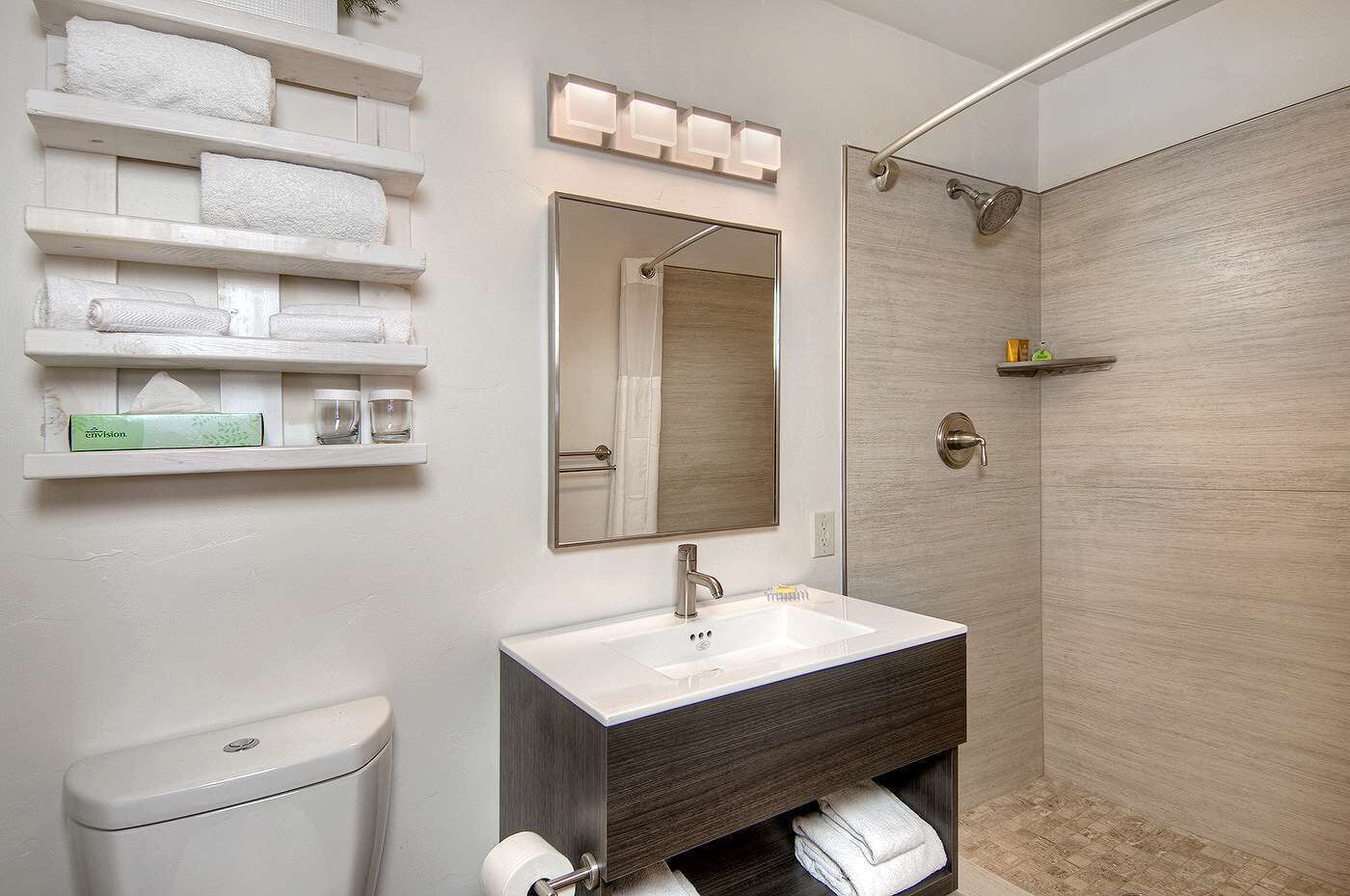 A modern bathroom with a white toilet, a sink with a dark wooden vanity, a mirror above the sink, and a shower area.