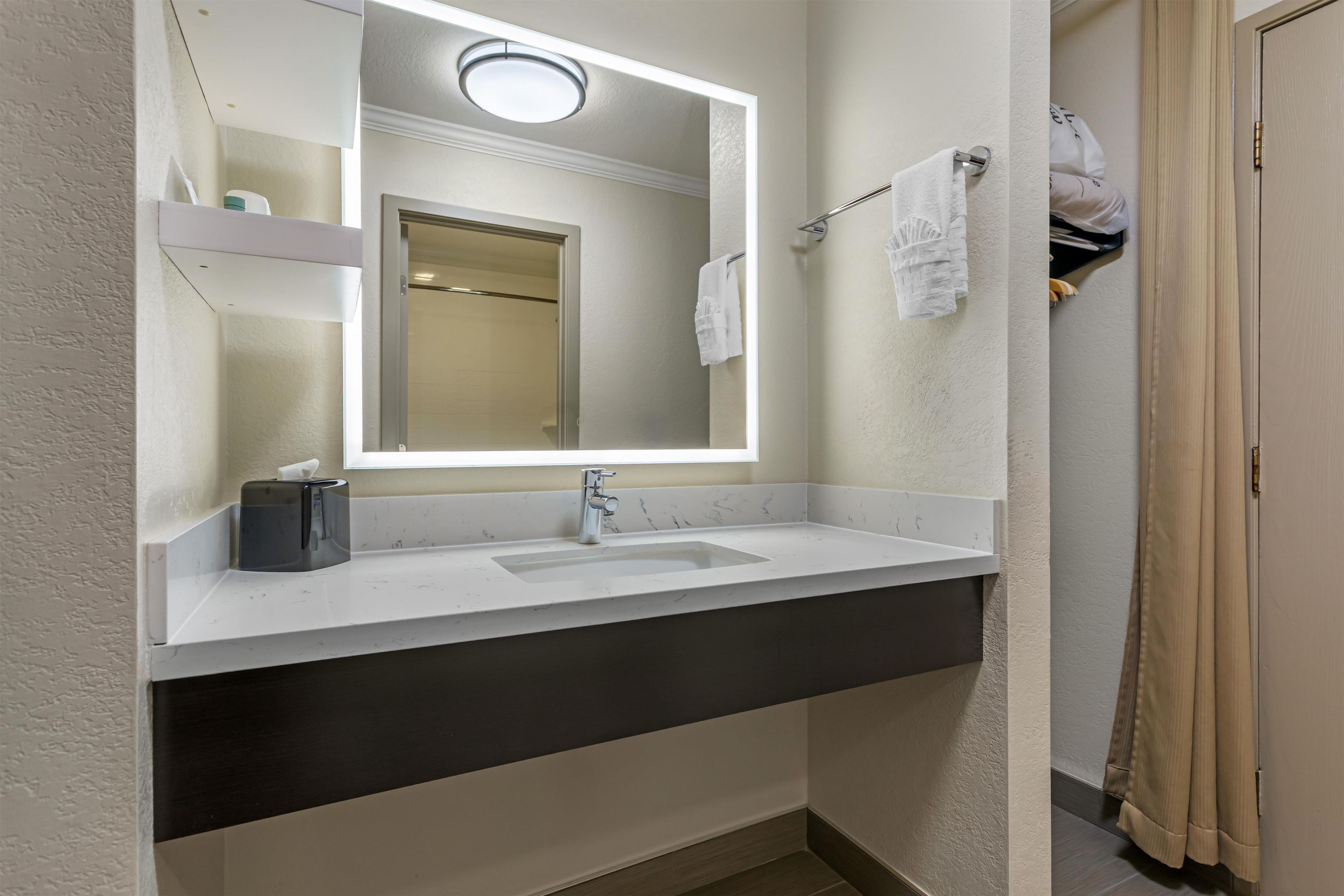 A bathroom with a white sink, a mirror with a light, a towel rack, and a shower curtain.