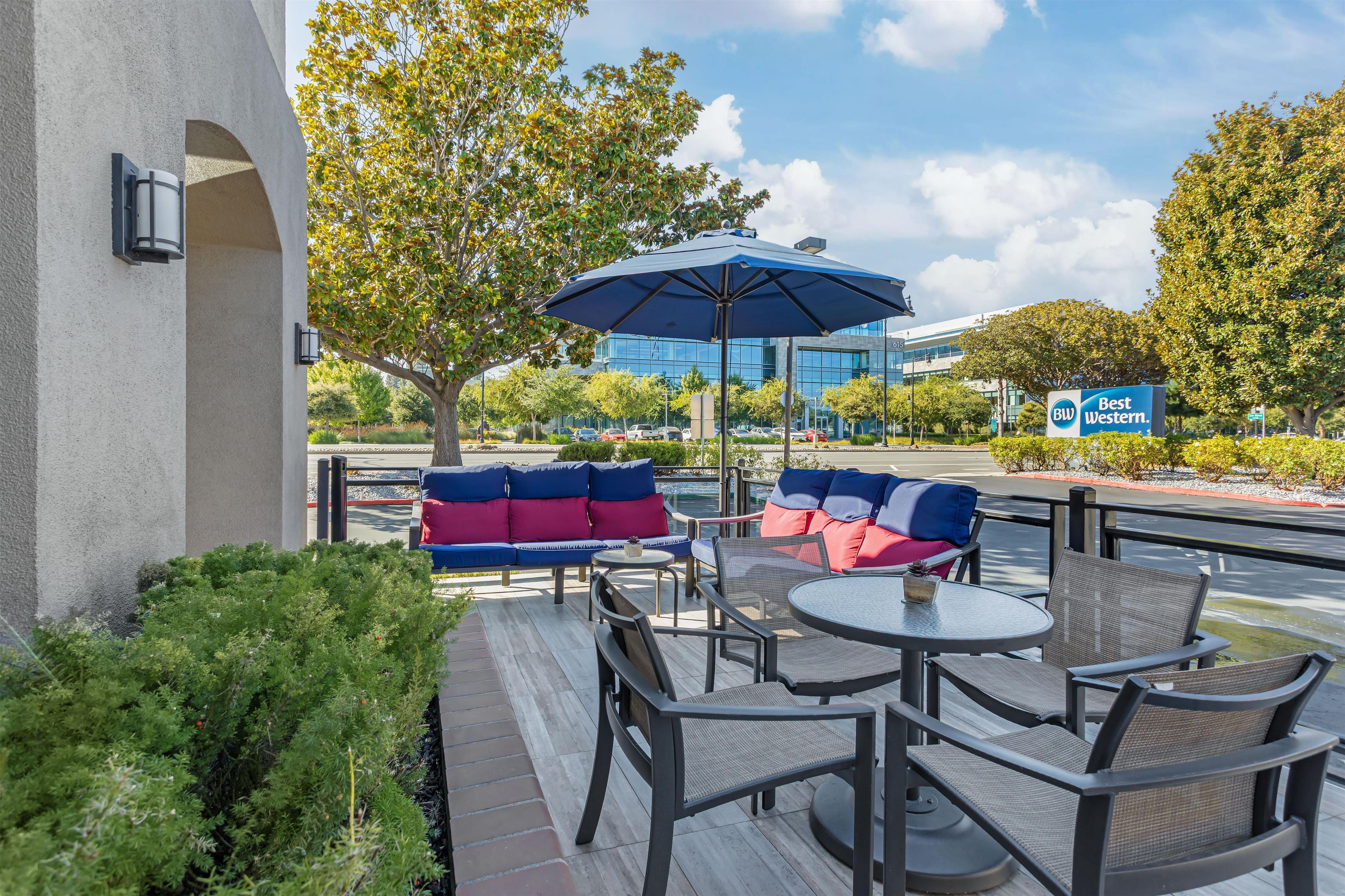 An outdoor seating area with a blue umbrella, wicker chairs, and a sofa with red and blue cushions.