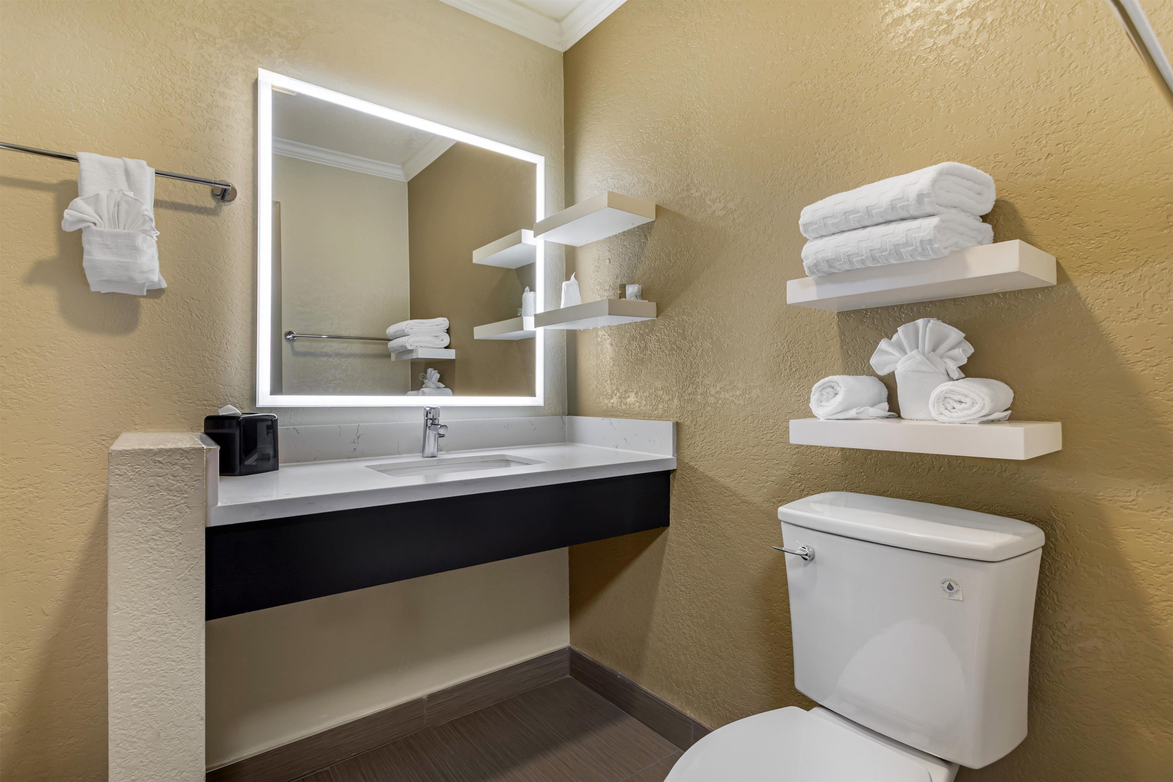 A bathroom with a white sink, a mirror, a toilet, and towel storage on shelves.