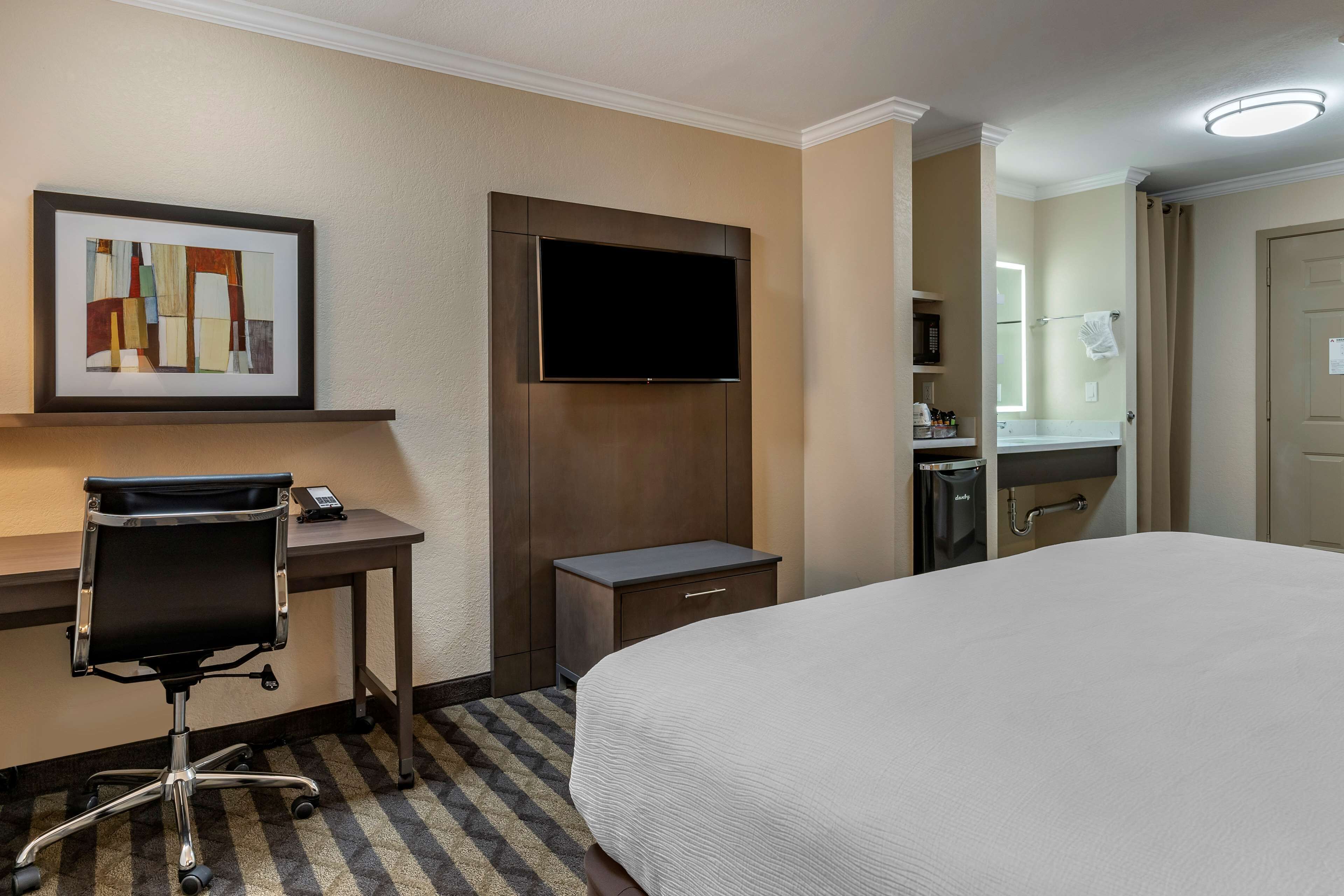 Una habitación de hotel con cama, escritorio, silla, televisor y baño pequeño.