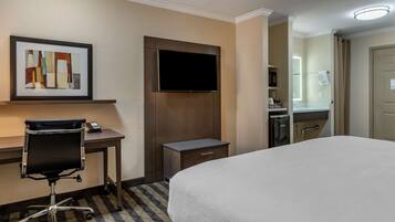 Una habitación de hotel con cama, escritorio, silla, televisor y baño pequeño.