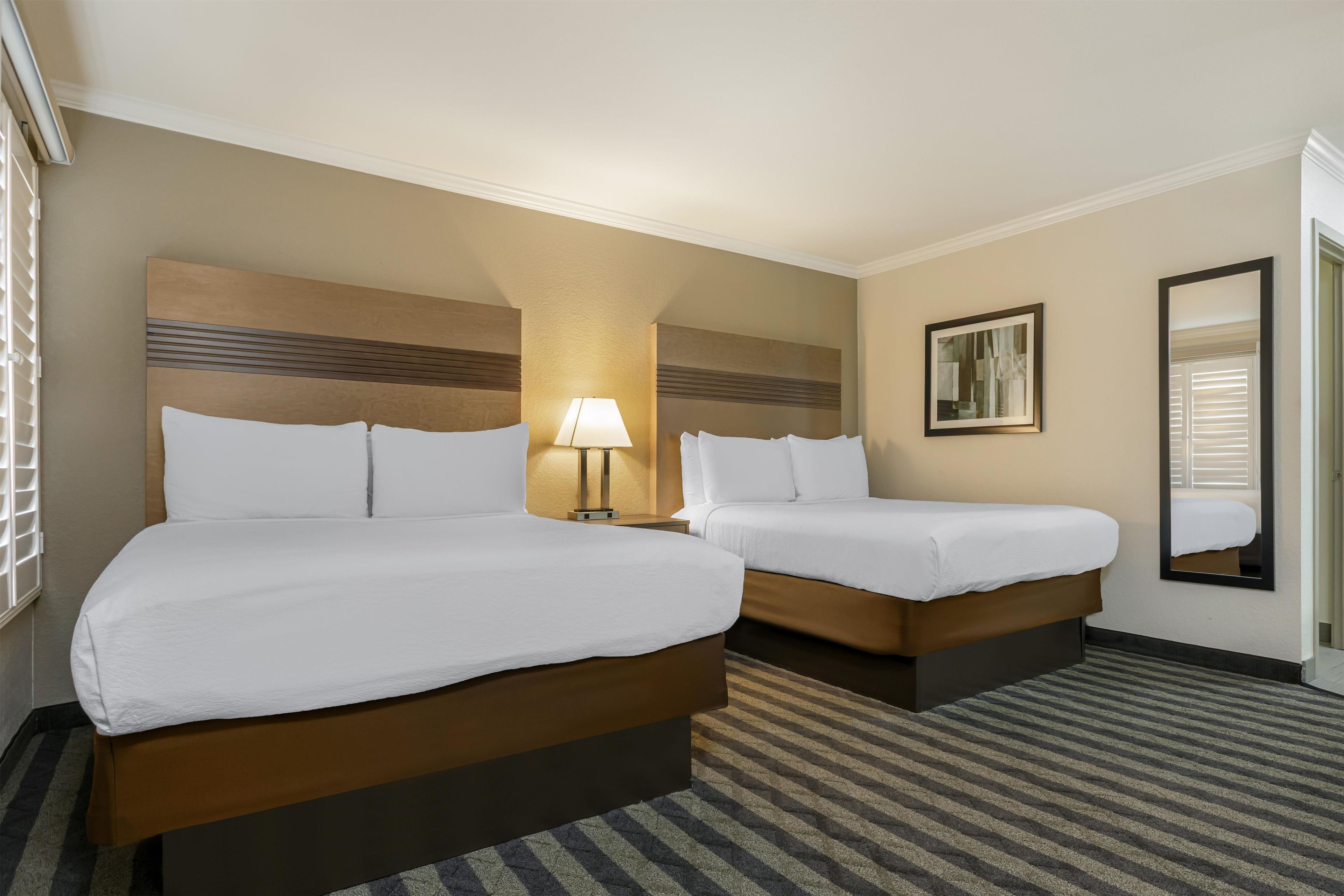 A hotel room with two beds, a lamp, a framed picture, and a mirror.