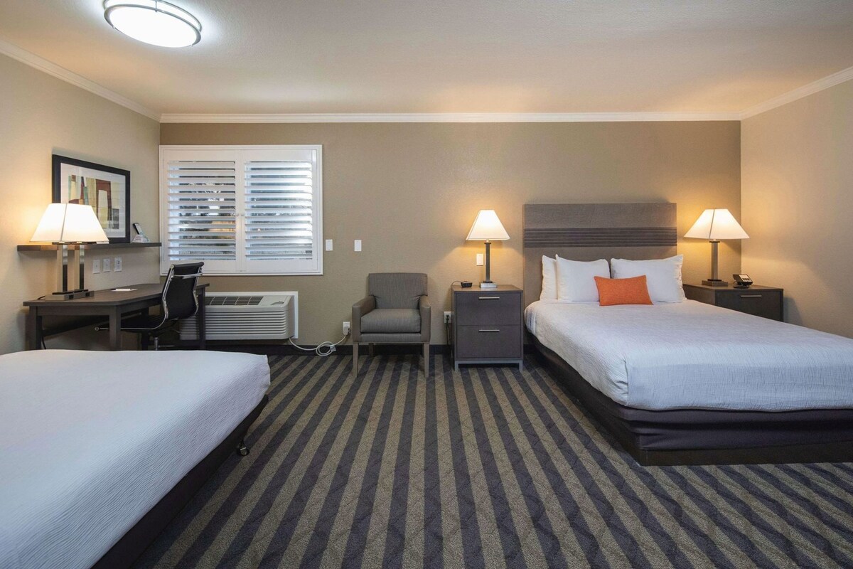 Une chambre d’hôtel avec deux lits, un bureau, une chaise, une petite table et un radiateur fixé au mur.