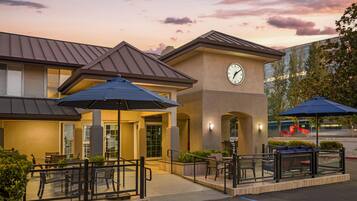A hotel exterior with outdoor seating, a clock, and a parking lot.