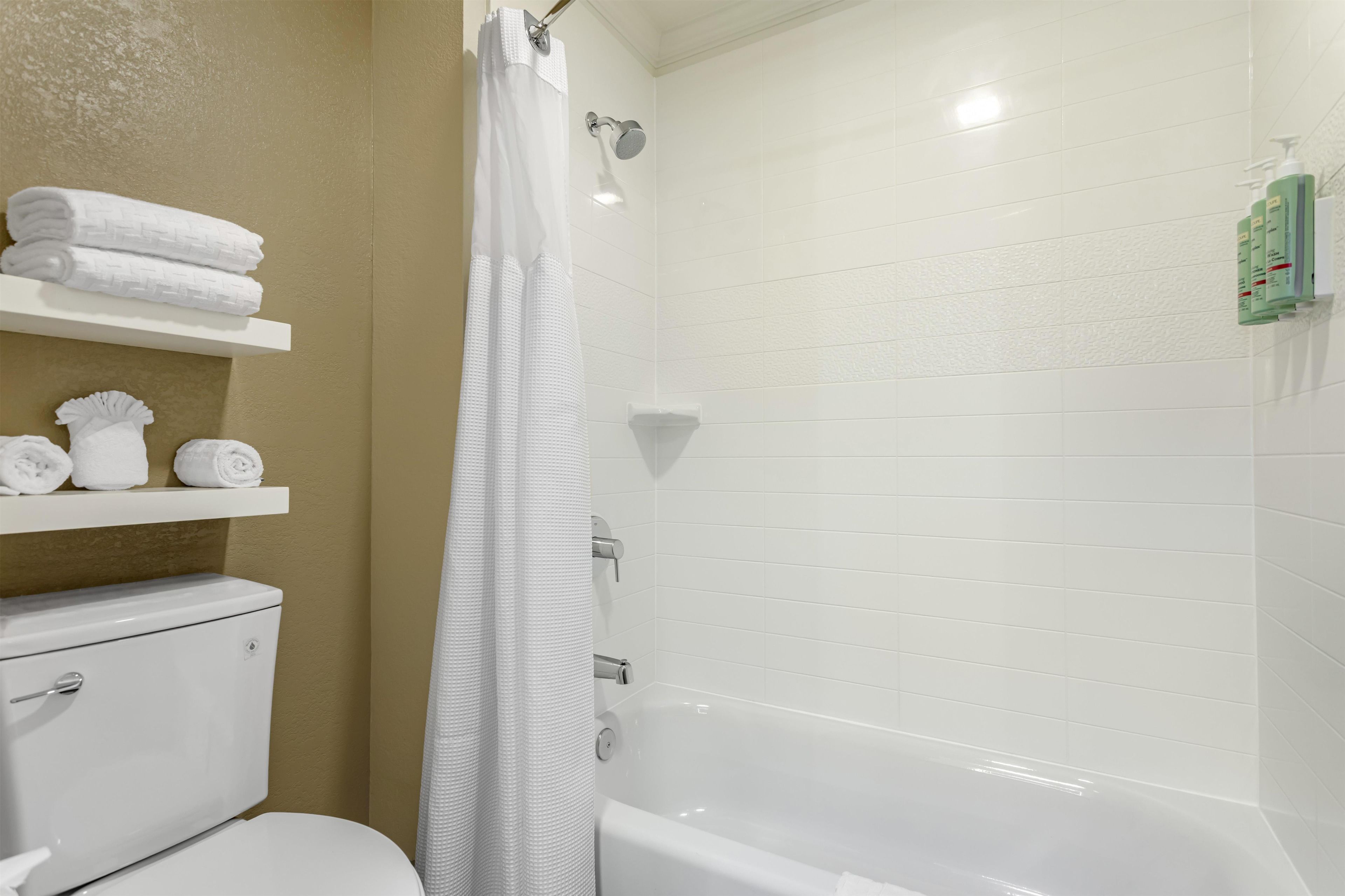 Un bagno con il WC, una doccia con tenda bianca e scaffali con asciugamani piegati.