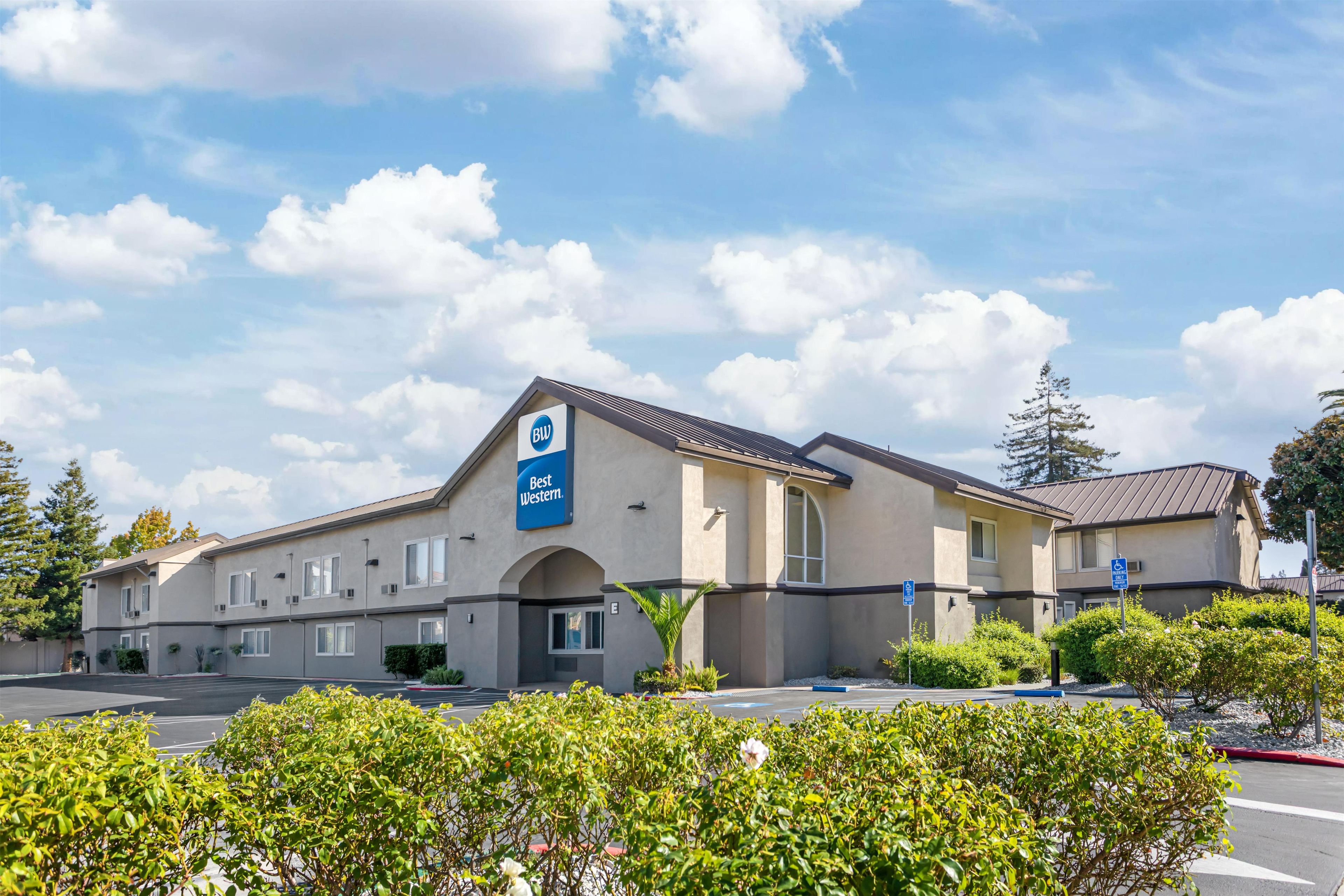 A hotel with a sign indicating it is part of the Best Western chain, featuring a parking lot and well-maintained landscaping.