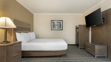 A hotel room with a bed, a desk, a chair, a TV, and a painting on the wall.