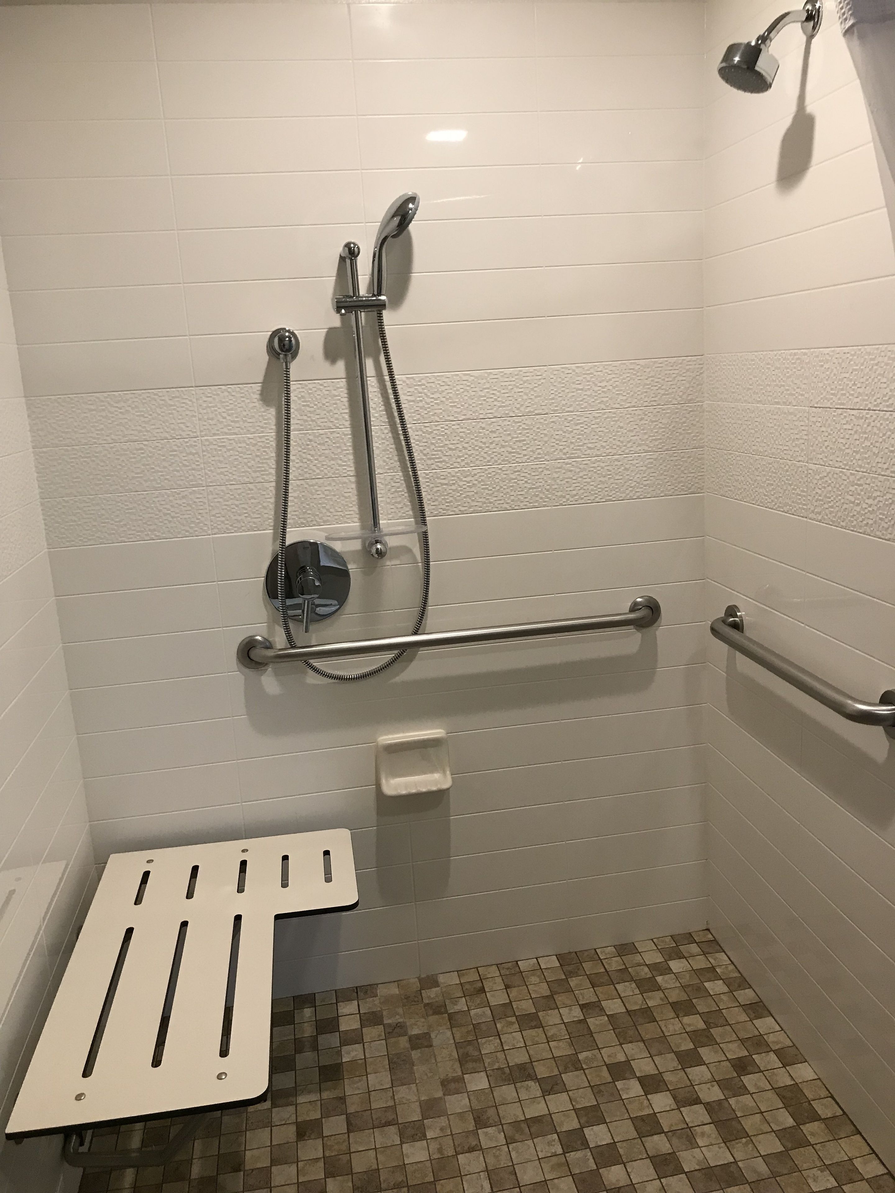 Pequeño espacio de ducha con azulejos, barra de apoyo y ducha de mano.
