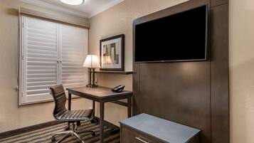 A hotel room with a desk, chair, lamp, TV, and a cabinet.