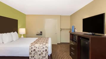 Una habitación de hotel con cama, televisor, un escritorio pequeño con lámpara y una puerta.