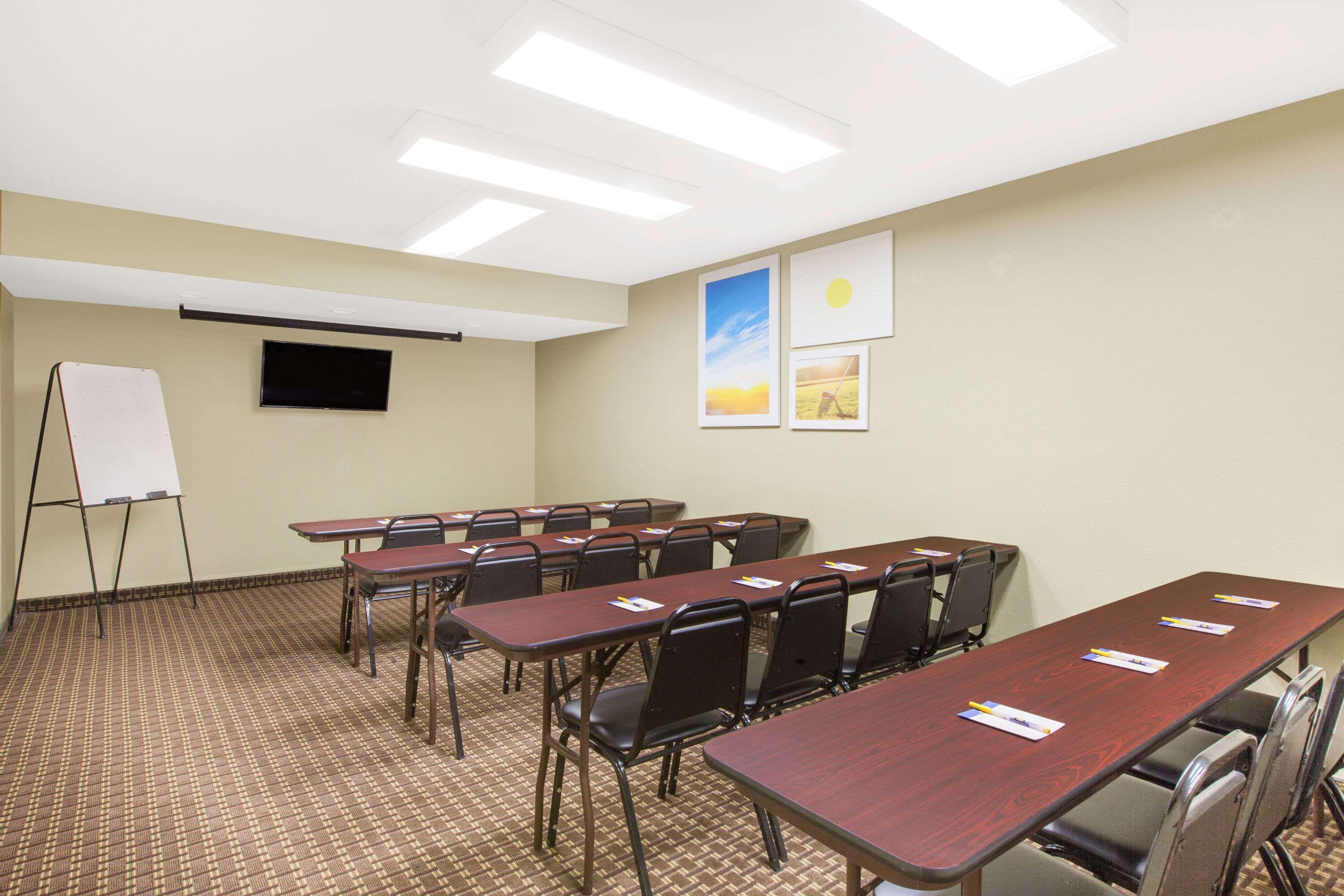 A conference room with multiple tables and chairs, a whiteboard, and a flat-screen TV on the wall.