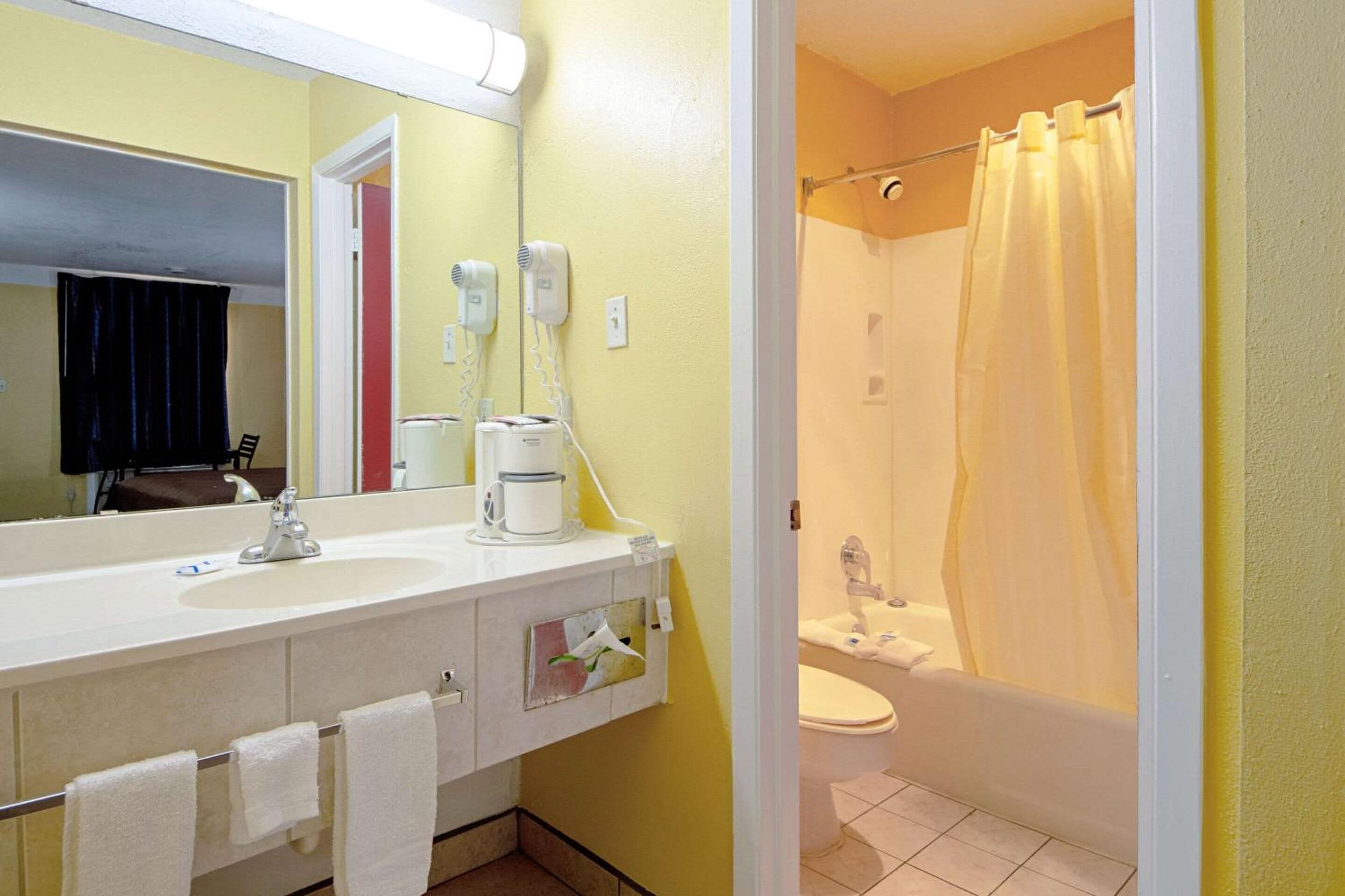 Un bagno con lavandino, specchio, asciugacapelli e tenda doccia.